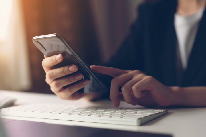 a man holding a phone while staring at his laptop